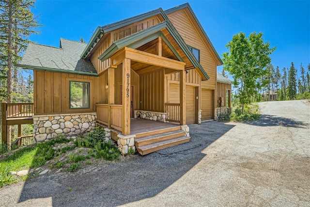 exterior space featuring board and batten siding, driveway, stone siding, and a shingled roof