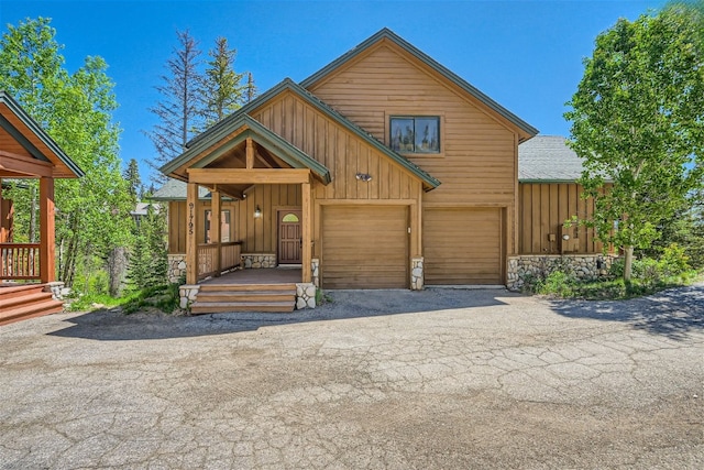 rustic home featuring aphalt driveway, stone siding, board and batten siding, and a garage