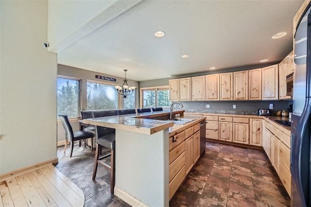 kitchen featuring light brown cabinets, a sink, a breakfast bar area, an inviting chandelier, and stainless steel appliances