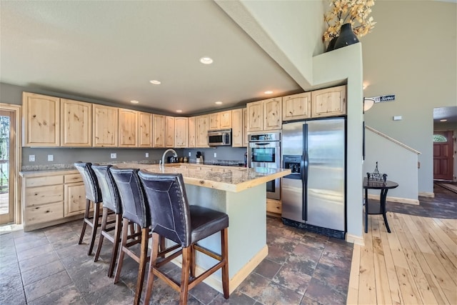 kitchen with stainless steel appliances, a kitchen breakfast bar, recessed lighting, light brown cabinets, and an island with sink