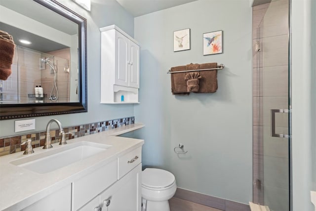 bathroom featuring a shower stall, toilet, vanity, baseboards, and decorative backsplash