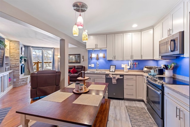 kitchen with a sink, stainless steel appliances, light wood finished floors, light countertops, and decorative light fixtures