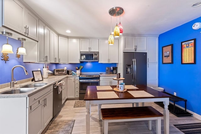 kitchen with light wood finished floors, a sink, light countertops, decorative light fixtures, and appliances with stainless steel finishes
