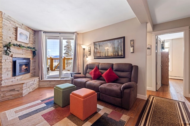 living room with a baseboard heating unit, a stone fireplace, hardwood / wood-style floors, and baseboards
