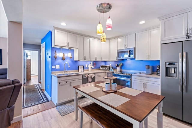kitchen with a sink, hanging light fixtures, appliances with stainless steel finishes, white cabinetry, and recessed lighting
