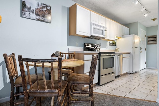 2883 Burgess Creek Rd Unit 203, Steamboat Springs, CO 80487 - kitchen with appliances with stainless steel finishes, rail lighting, white cabinetry, and light tile patterned floors