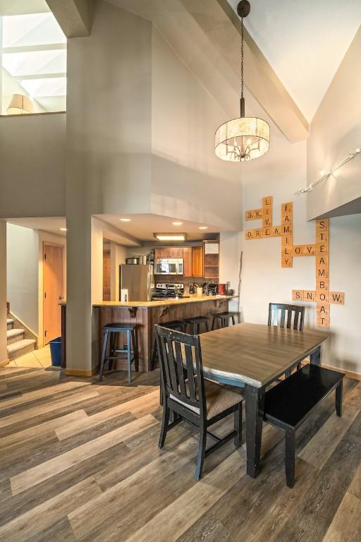 2800 Village Dr Unit 1302, Steamboat Springs, CO 80487 - dining space featuring high vaulted ceiling, wood finished floors, a chandelier, stairs, and baseboards