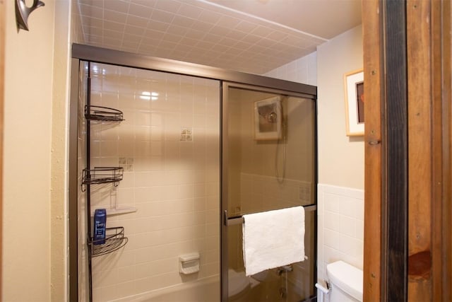 bathroom featuring wainscoting, combined bath / shower with glass door, and toilet