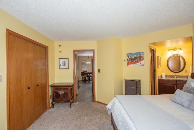 bedroom featuring light colored carpet, connected bathroom, a textured ceiling, and a closet