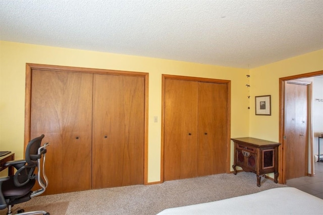 carpeted bedroom with a textured ceiling and multiple closets