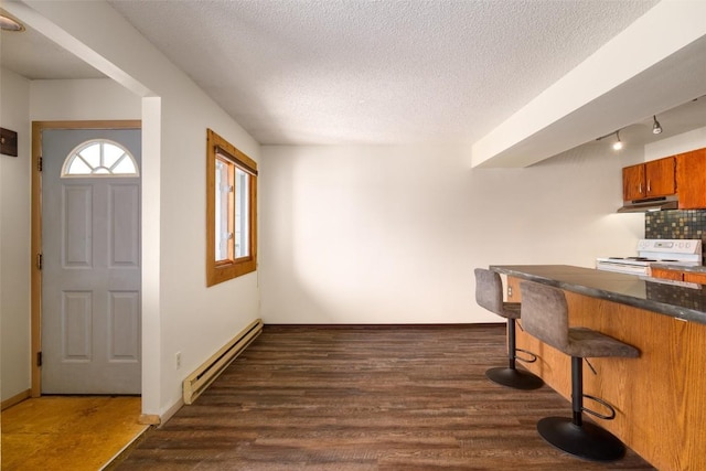 13 Sequoia Ct Unit 13, Steamboat Springs, CO 80487 - kitchen featuring white electric stove, a kitchen breakfast bar, under cabinet range hood, dark countertops, and a baseboard radiator