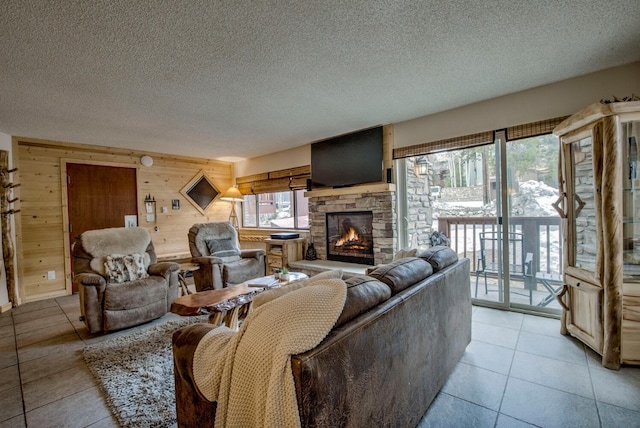 living room featuring a stone fireplace, wooden walls, light tile patterned flooring, and a textured ceiling