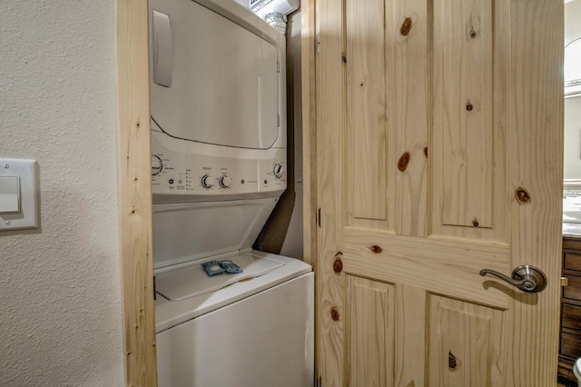 clothes washing area with laundry area, a textured wall, and stacked washer and dryer