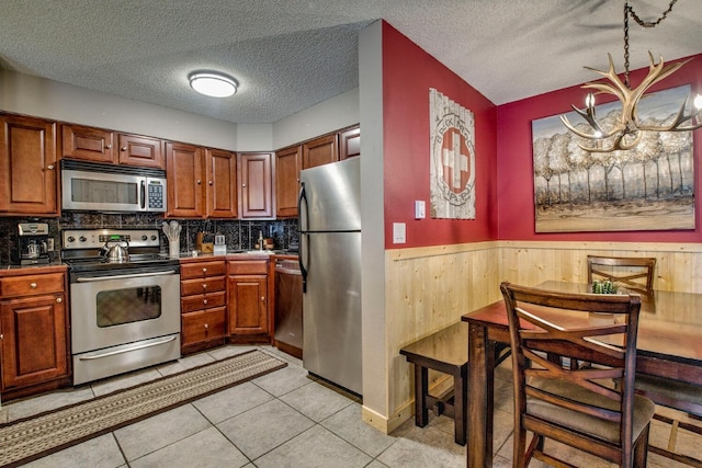 kitchen with stainless steel appliances, brown cabinetry, a textured ceiling, wood walls, and wainscoting