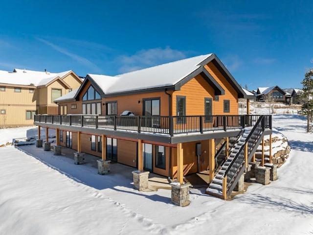 snow covered rear of property with an attached garage, stairway, and a deck