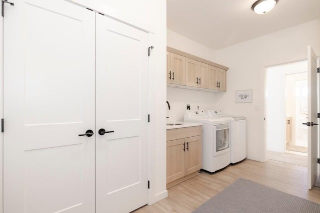 laundry room with washing machine and dryer, a sink, light wood finished floors, and cabinet space