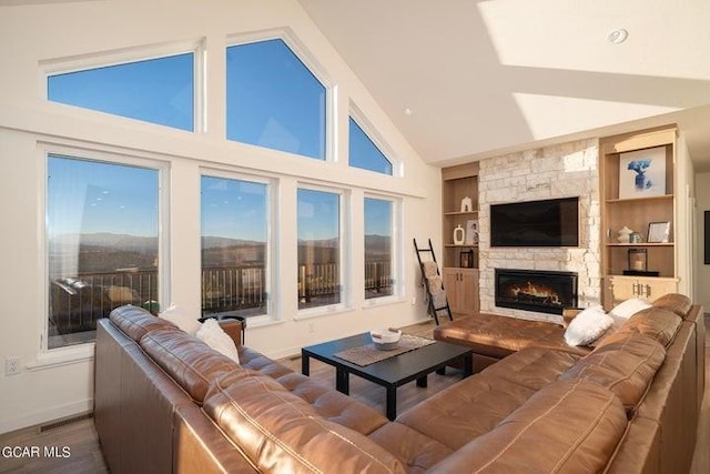 living area featuring wood finished floors, a stone fireplace, built in shelves, baseboards, and lofted ceiling