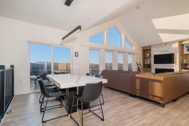 living area featuring vaulted ceiling, a stone fireplace, light wood-type flooring, baseboards, and built in features