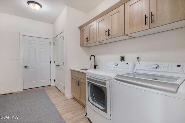 washroom featuring separate washer and dryer, cabinet space, a sink, and light wood-style flooring