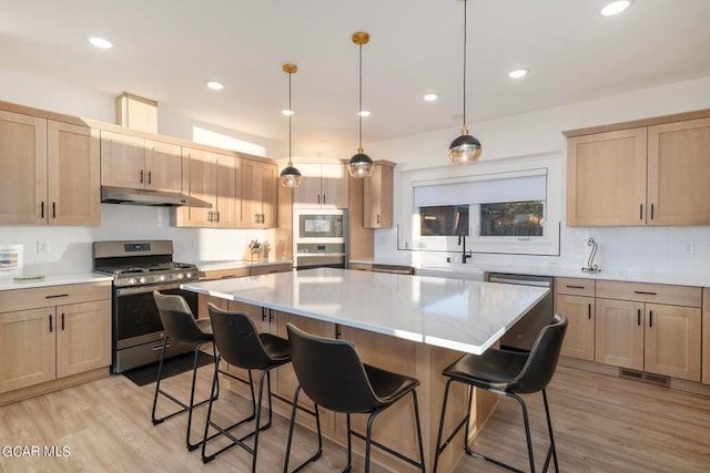 kitchen with light wood-type flooring, stainless steel appliances, a kitchen breakfast bar, and under cabinet range hood