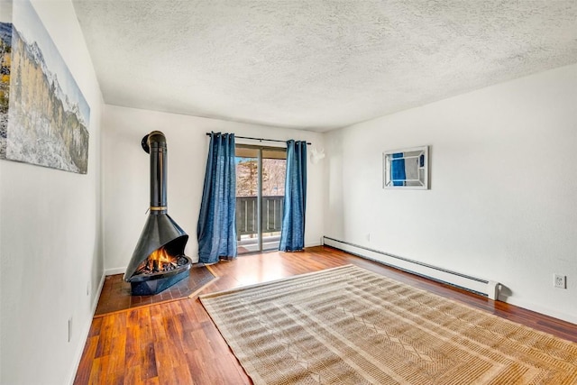 interior space featuring a textured ceiling, baseboard heating, a wood stove, and wood finished floors