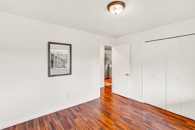 unfurnished bedroom featuring a closet, freestanding refrigerator, baseboards, and wood finished floors