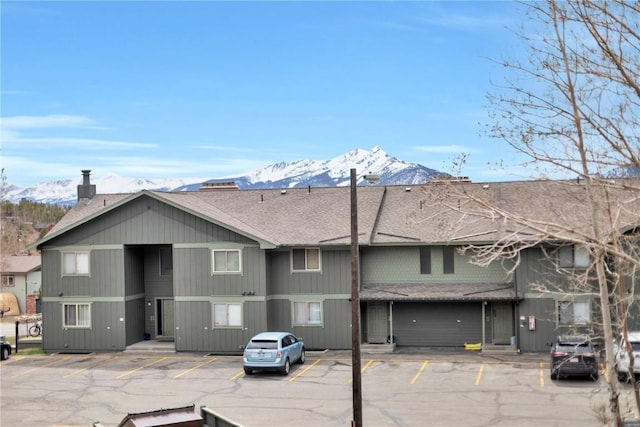 exterior space with a shingled roof, uncovered parking, a mountain view, and a chimney