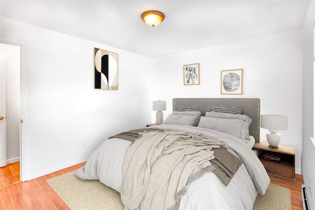 bedroom with baseboards, a baseboard heating unit, and light wood finished floors