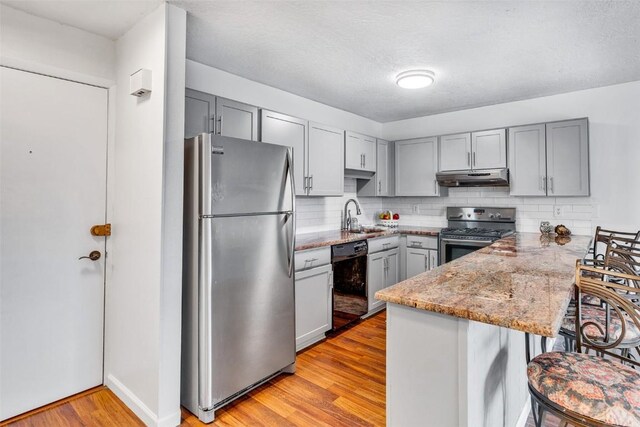 kitchen with gray cabinets, a sink, a peninsula, under cabinet range hood, and stainless steel appliances