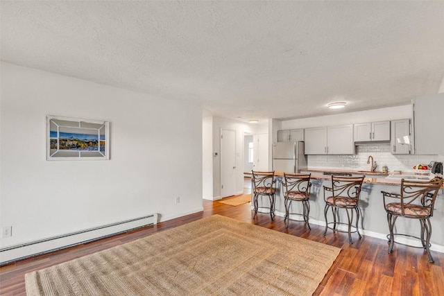 kitchen featuring baseboard heating, a breakfast bar area, freestanding refrigerator, a peninsula, and gray cabinetry