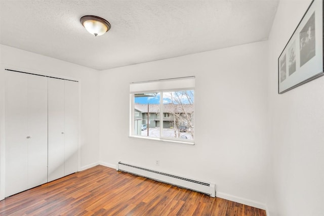 unfurnished bedroom featuring a textured ceiling, baseboard heating, wood finished floors, baseboards, and a closet