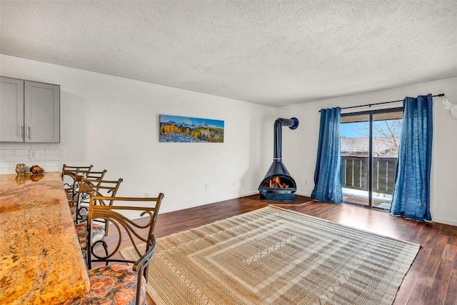 unfurnished bedroom with a wood stove, access to exterior, baseboards, dark wood-type flooring, and a textured ceiling