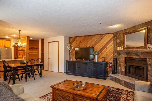 living area with light carpet, a textured ceiling, a notable chandelier, wooden walls, and a stone fireplace