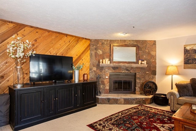 living area featuring wood walls, a stone fireplace, a textured ceiling, and carpet