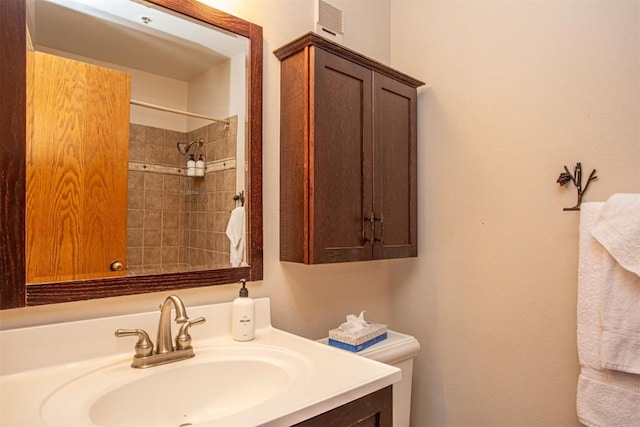 bathroom featuring toilet, vanity, visible vents, and tiled shower