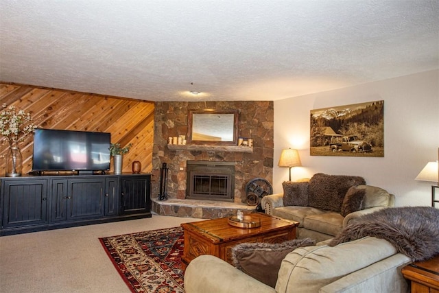 carpeted living area with wooden walls, a stone fireplace, and a textured ceiling