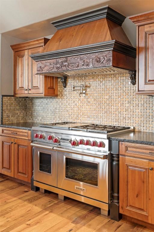 174 Sage Dr, Breckenridge, CO 80424 - kitchen featuring brown cabinetry, backsplash, double oven range, dark countertops, and custom exhaust hood