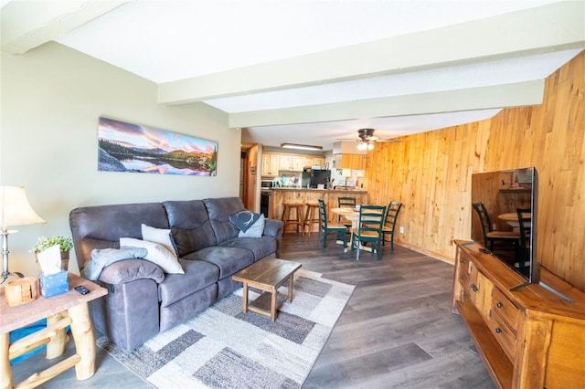 living area with dark wood-type flooring, beam ceiling, wood walls, and ceiling fan
