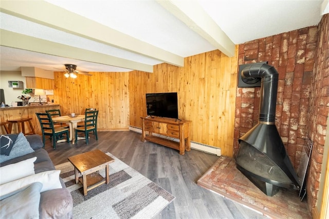 living room with wood finished floors, a wood stove, a baseboard heating unit, beam ceiling, and baseboard heating