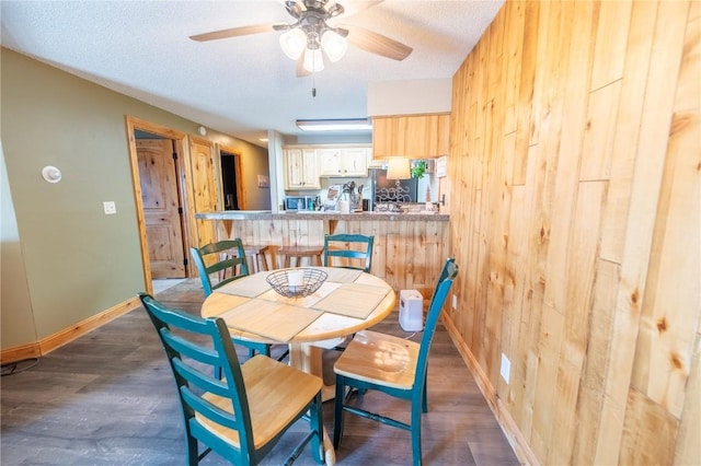 dining area with wood walls, wood finished floors, baseboards, and ceiling fan