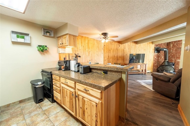 kitchen featuring wood walls, a wood stove, a peninsula, electric range, and ceiling fan