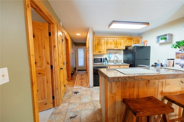 kitchen featuring a textured ceiling, a sink, a breakfast bar area, and black appliances