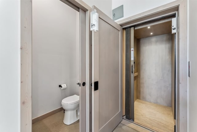 bathroom with concrete floors, elevator, and toilet