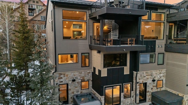 back of property with stone siding, a standing seam roof, a balcony, and board and batten siding