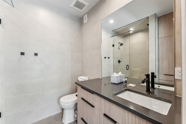 bathroom with a stall shower, vanity, tile walls, toilet, and visible vents