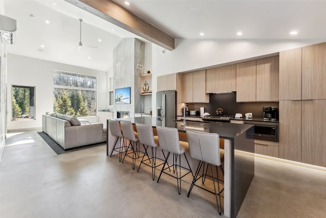 kitchen featuring light brown cabinets, modern cabinets, a kitchen bar, appliances with stainless steel finishes, and high vaulted ceiling