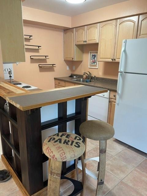 kitchen with a sink, light tile patterned flooring, light brown cabinetry, dark countertops, and freestanding refrigerator