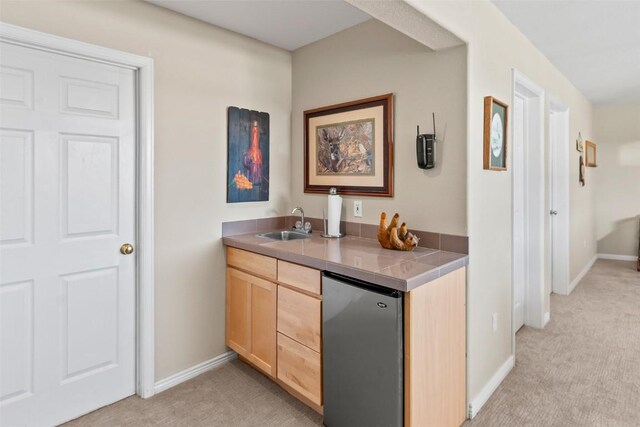 bar featuring light carpet, a sink, fridge, baseboards, and indoor wet bar
