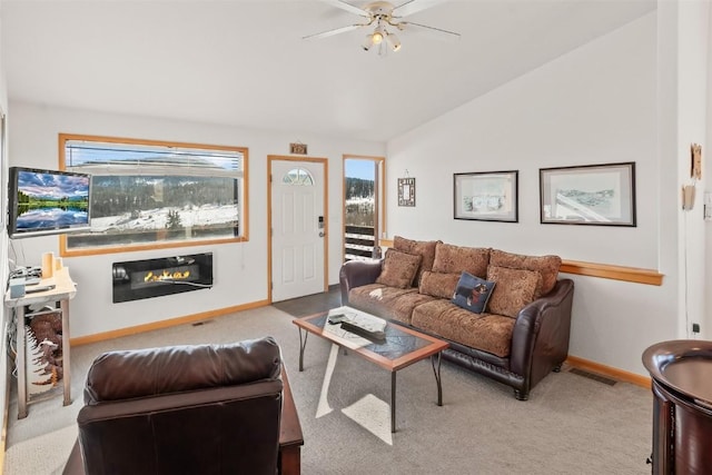 carpeted living area featuring vaulted ceiling, a glass covered fireplace, ceiling fan, baseboards, and visible vents