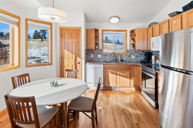 kitchen featuring light wood finished floors, a sink, decorative backsplash, open shelves, and appliances with stainless steel finishes